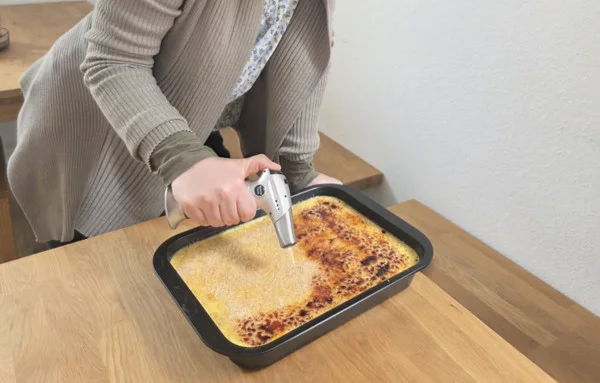 Die Kollegin flambiert die Karamellkruste der Crème brûlée.